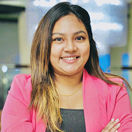 A woman wearing a pink blazer smiles at the camera with her arms crossed.